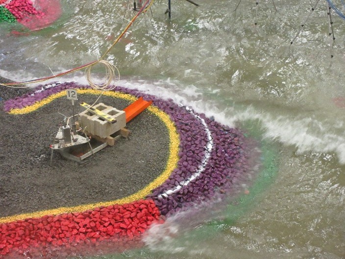 Photograph of a measurement tool surrounded by coloured rocks in a scaled physical model of a coastal region in a research laboratory.