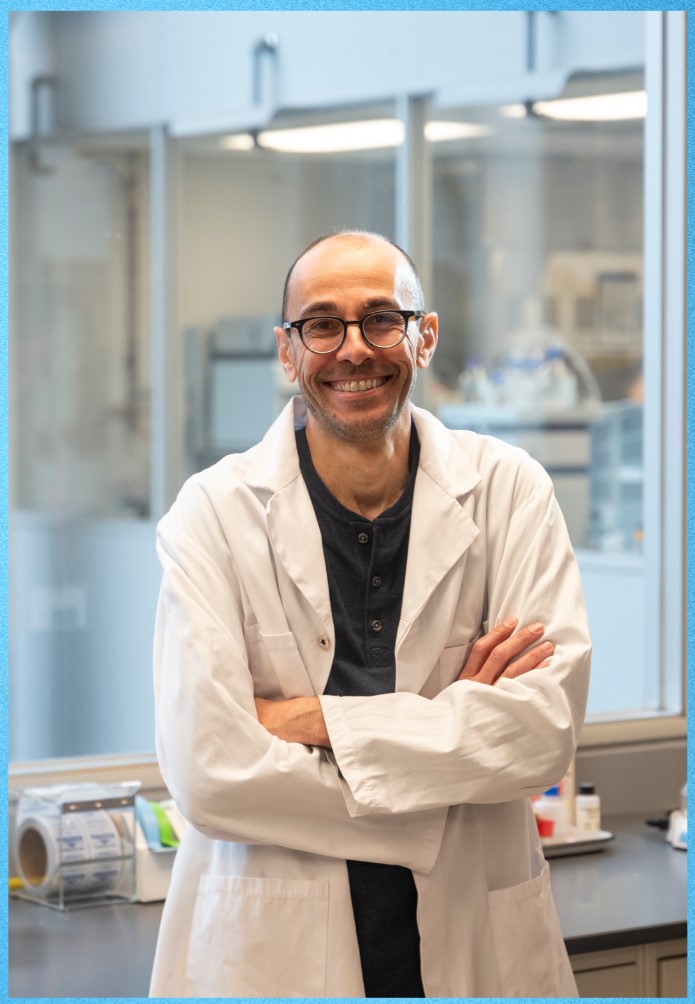 Man in white lab coat, arms across his chest smiling to camera. 