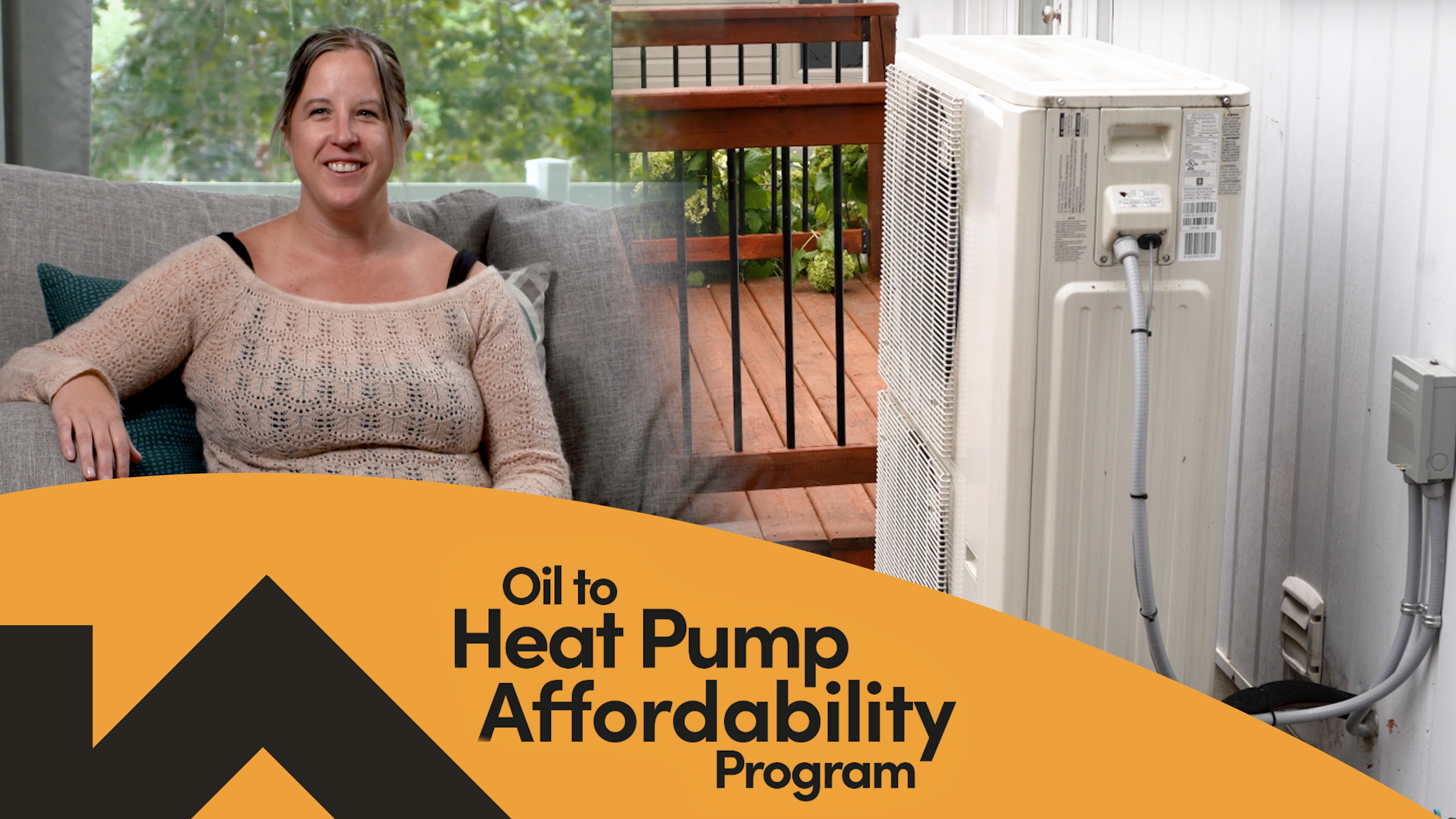 A smiling woman rests her arm on a heat pump on a metal stand next to her home