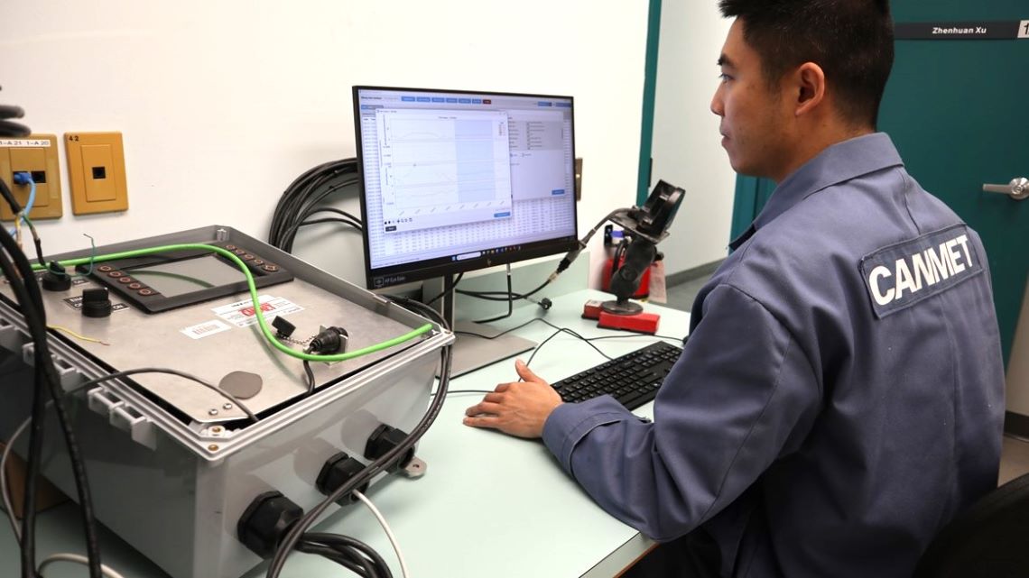 A scientist using a computer connected to electronic equipment to examine data at a laboratory workstation. 