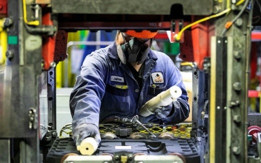 A worker in protective gear operates machinery on an industrial production line.