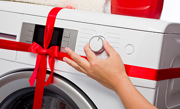 Someone changes settings on their new washing machine that is wrapped with a bow.