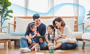 Family sitting together on the floor of their living room, the father is holding a tablet in his hands.