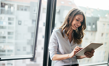 Young businesswoman using a digital tablet while standing in front of windows in office.