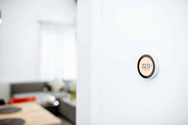 Round smart thermostat with touch screen installed on the wall indoors.