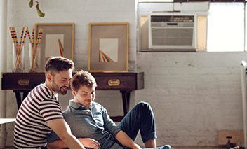 Couple in living room, window AC unit mounted in background.