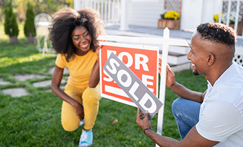 Young couple who recently purchased a house places SOLD sign on top of the FOR SALE sign in the front yard.