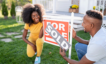 Jeune couple ayant récemment acheté une maison qui place le signe VENDU par-dessus le signe À VENDRE dans leur jardin.