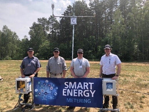 Four male colleagues stand in a field behind a banner that reads “Smart energy metering” along with the tools developed during the project.