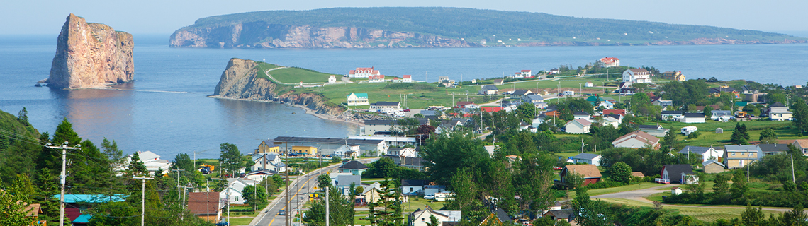 View of the coastal village of Percé, Quebec, with a sheer rock formation to the left (Percé Rock) and Bonaventure Island in the background.