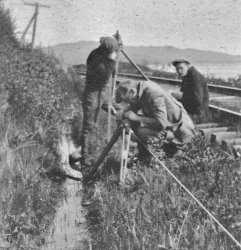 Technicians taking measurements with a precise traverse on the side of a railroad track in a ditch