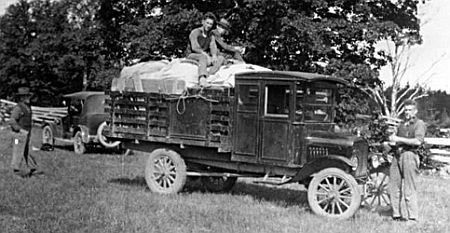Motorized truck in a field with technicians standing around and on top of the truck with car in the background