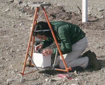 Technician kneeling on the rocky ground taking measurements with a Lacoste-Romberg gravimeter