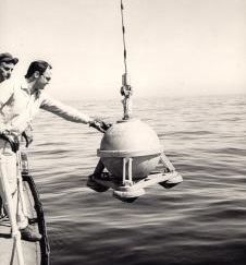 Gravimeter being lowered into the water with technician on a boat steering the equipment