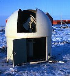 Surveying equipment in a dome on snow with a building in the background