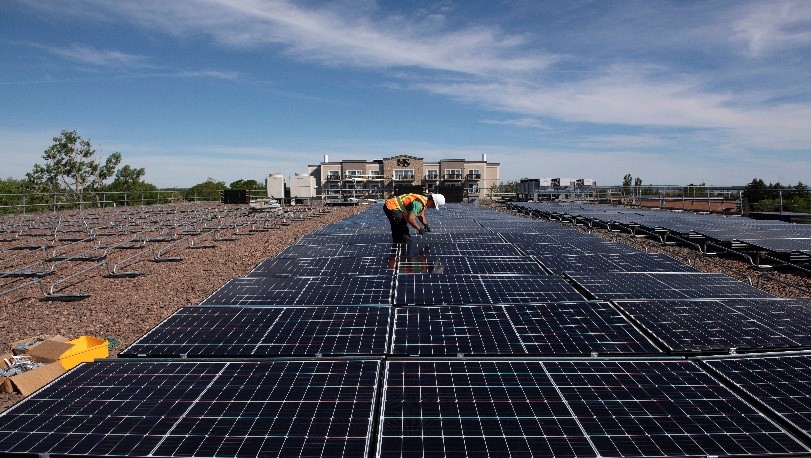 A field technician inspects a large array of rooftop solar panels.