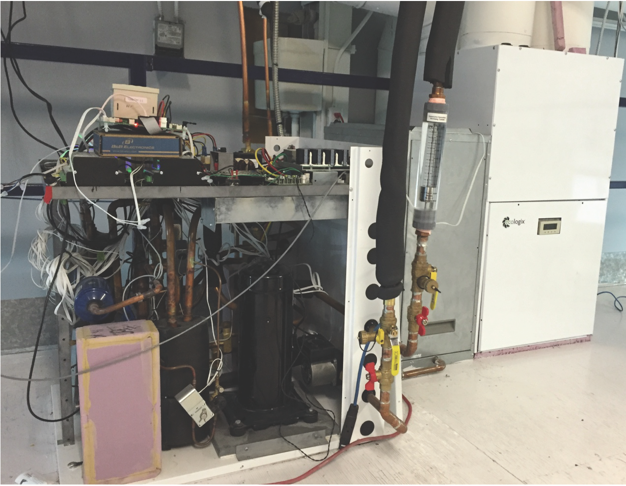 The photo shows the interior of the Ecologix prototype integrated heat pump module, connected to various instruments for laboratory testing, with its air handler in the background