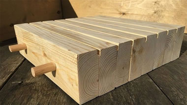 Two pieces of round doweling spaced apart, fitted perpendicularly through eight boards stacked parallel to each other.