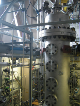 Image of a tall industrial metal cylinder with heavy bolts and various connections and gauges standing over 1.5 metres tall. 