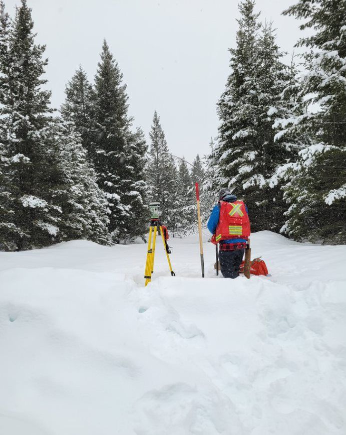 A person standing in the snow with surveying equipment