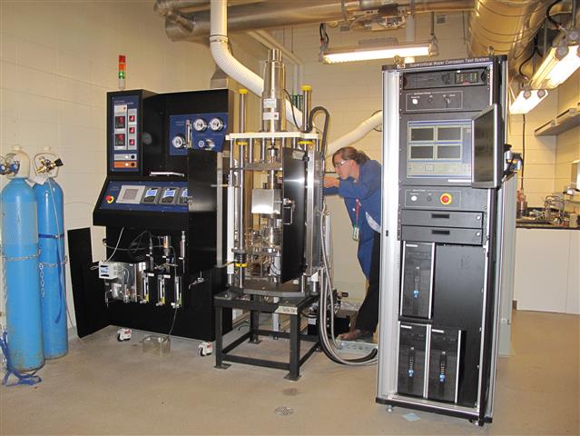 Woman using a machine in a high-temperature and high-pressure corrosion laboratory.