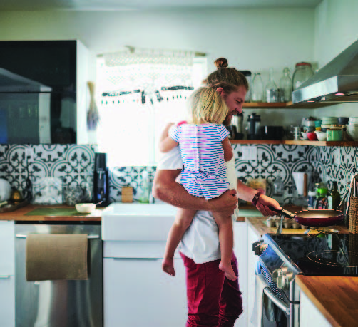 Father holding daughter in his arms while he cooks on an electric cooktop