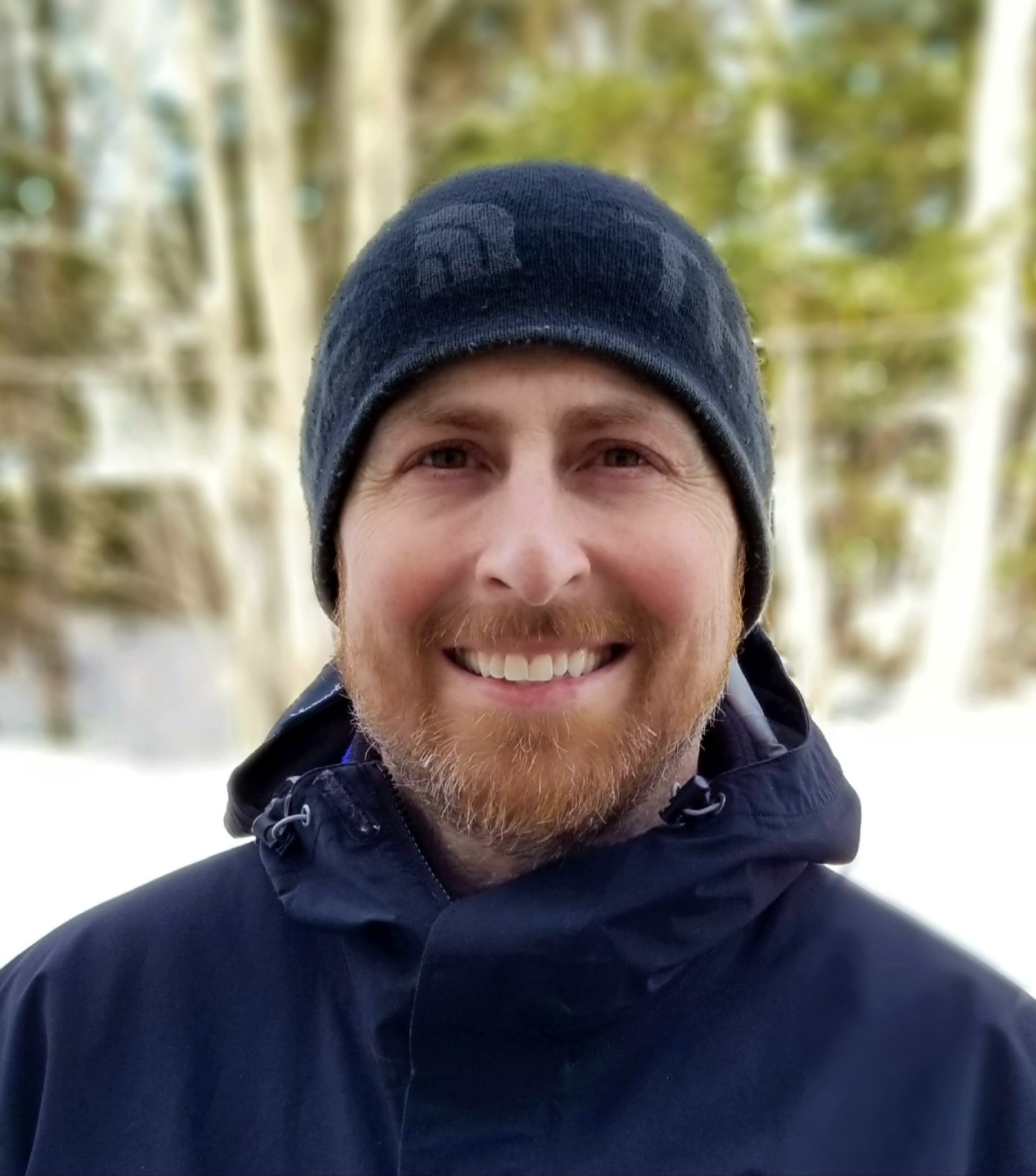 Photo of a smiling Guy Strickland wearing a ball cap with trees in the background.