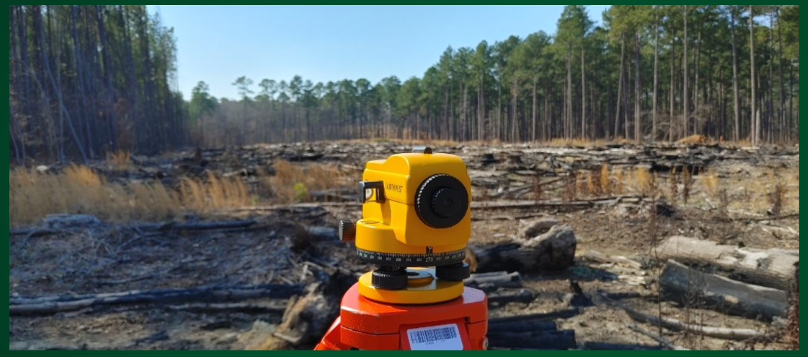 A theodolite with a broad open forested area in the background.