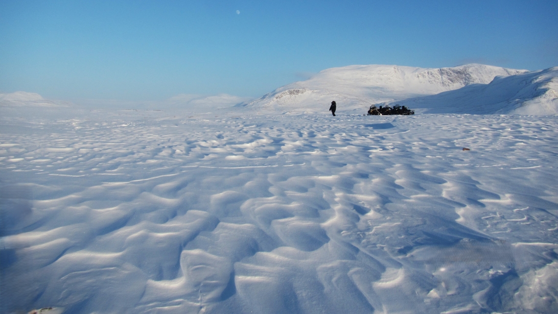 A person with a snowmobile loaded with gear on the frozen tundra.