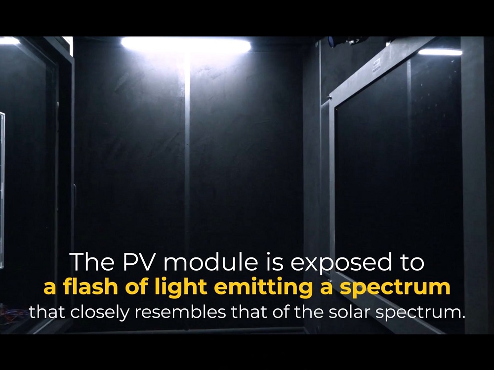 Inside dark chamber solar panel is exposed to flash of light. On screen text: The PV module is exposed to a flash of light emitting a spectrum that closely resembles that of the solar spectrum.